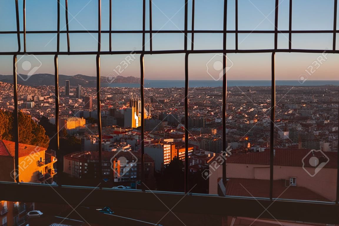 A scenic cityscape of Barcelona through a metal lattice window, view from Bunkers del Carmel (Colina de la Rovira)