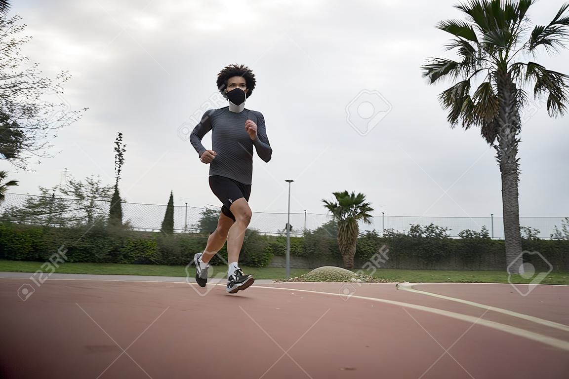 A shallow focus of a male athlete with a facemask jogging in a park in the morning