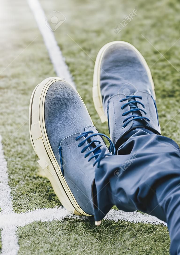 A vertical shot of a man wearing blue shoes with crossed legs on grass