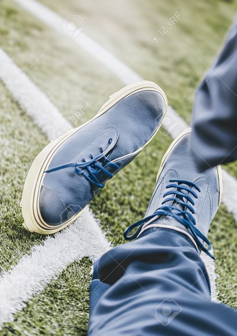 A vertical shot of a man wearing blue shoes with crossed legs on grass