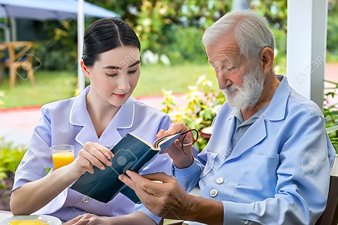 Anciano Senior libro de lectura con la enfermera durante el desayuno en el jardín en el hogar de ancianos