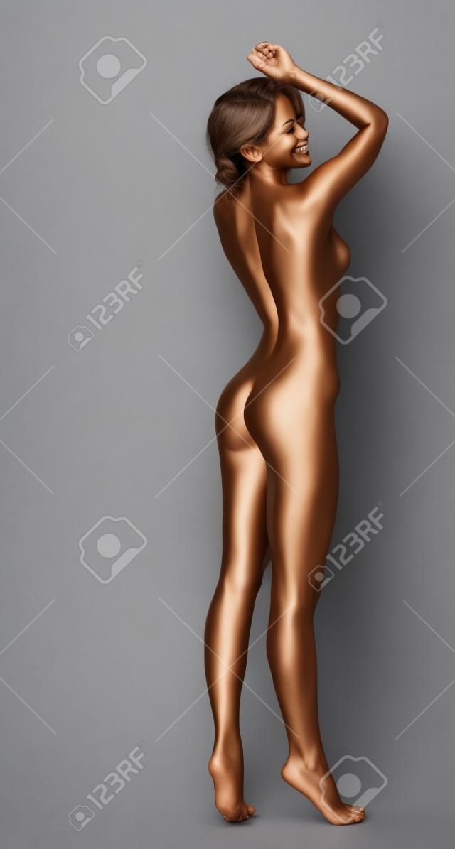 Smiling skinny bronzed woman posing in studio, on gray background