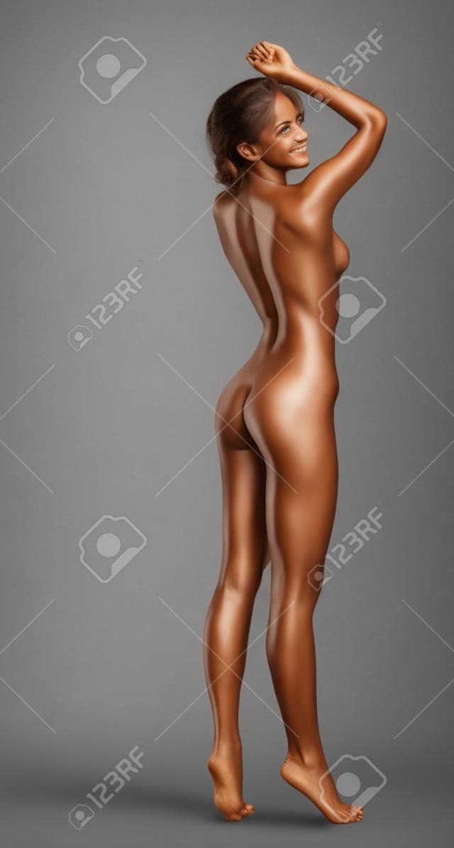 Smiling skinny bronzed woman posing in studio, on gray background