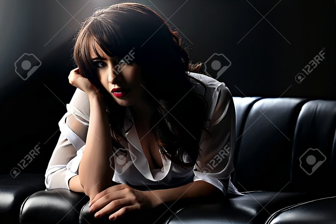 Portret brunetka w białej koszuli na kanapie