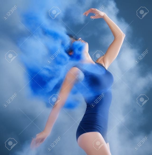 Slim girl dancing in blue dust cloud profile view