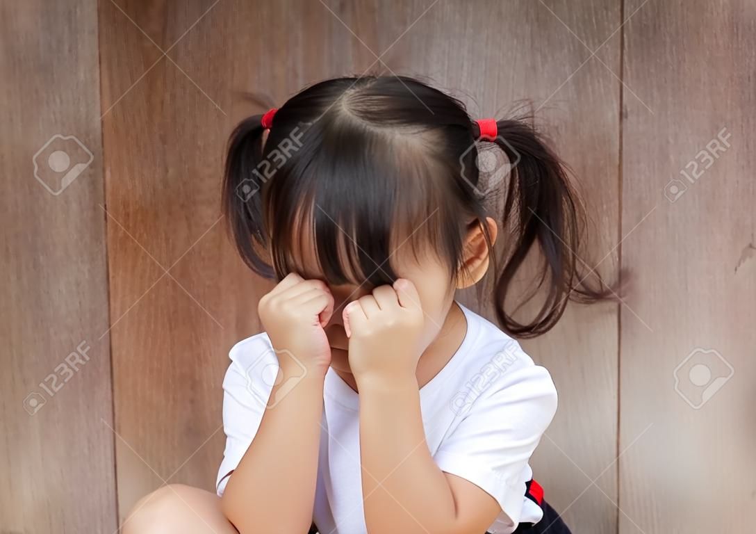 Portrait de la moitié du corps d'une adorable fille asiatique, âgée d'environ 4 ans avec une chemise blanche, qui pose un visage effronté, pleure, joue avec l'appareil photo sur l'arrière-plan flou d'une porte en bois vintage.