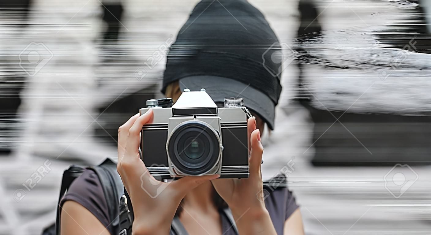 Geernteter Schuss des weiblichen gekleideten gekleideten Touristen mit einem Rucksack , der mit Retro- Filmkamera vor der Graffitiwand aufwirft . Reise- und freiberuflich Konzept . Kopieren Sie Platz für Ihren Text