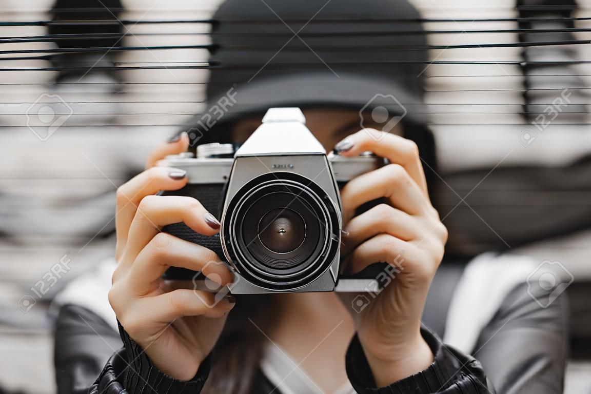 Colpo potato del turista con indifferenza vestito femminile con uno zaino che posa con la retro macchina fotografica della foto del film davanti alla parete dei graffiti. Concetto di viaggio e freelance.