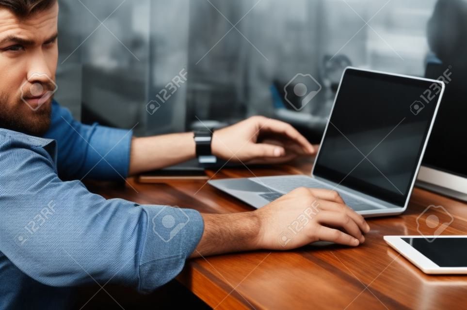 El hombre usa jeans usando una computadora portátil para un proyecto de negocios, un teléfono inteligente, un panel táctil, una computadora portátil
