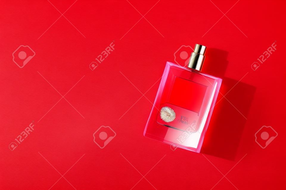 Transparent bottle of perfume with label on a red background. Fragrance presentation with daylight. Trending concept in natural materials palm leaves shadow. Womens and mens essence.