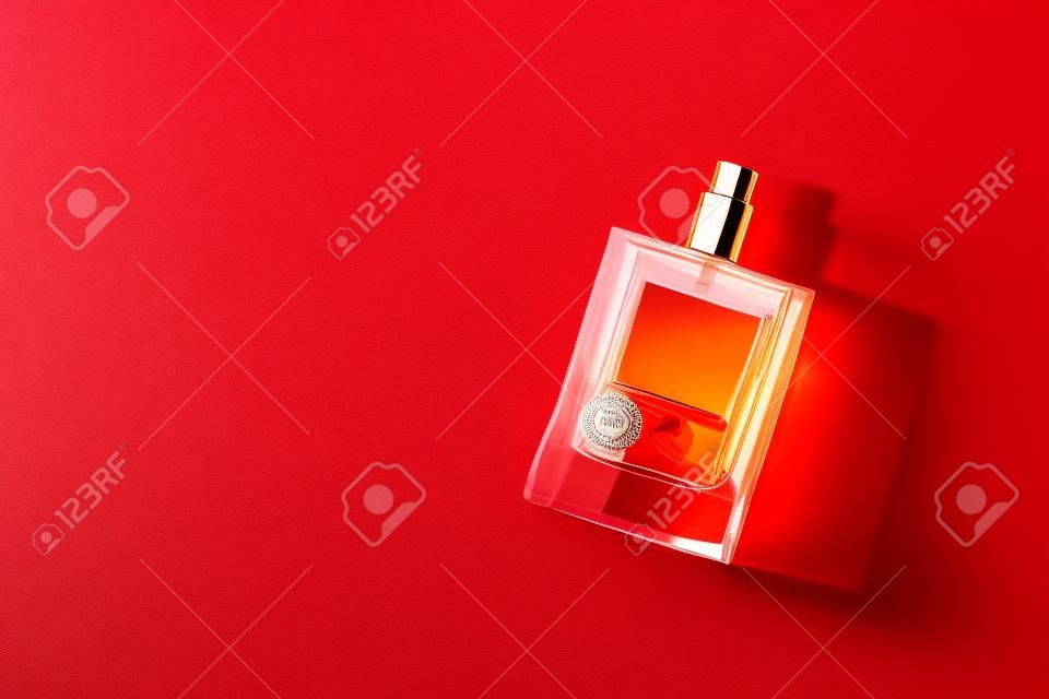 Transparent bottle of perfume with label on a red background. Fragrance presentation with daylight. Trending concept in natural materials palm leaves shadow. Womens and mens essence.