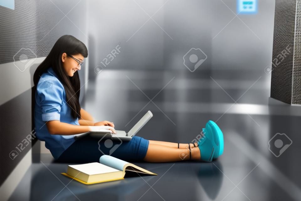 Female accounting student studying with laptop computer and textbook in campus aisle