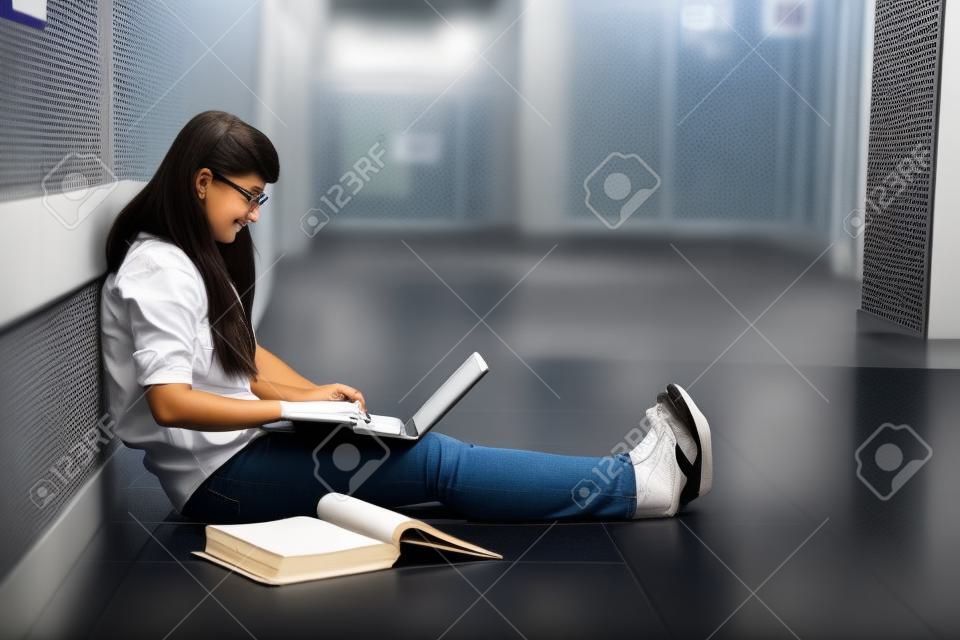 Female accounting student studying with laptop computer and textbook in campus aisle