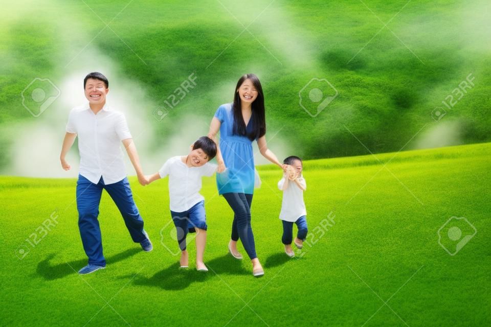 Familia feliz asiática runing juntos en prado tiro al aire libre