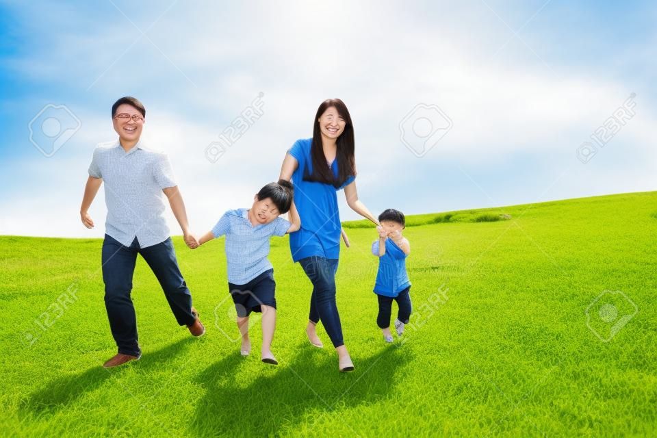 Szczęśliwa rodzina runing asian razem na łące zastrzelony na zewnątrz