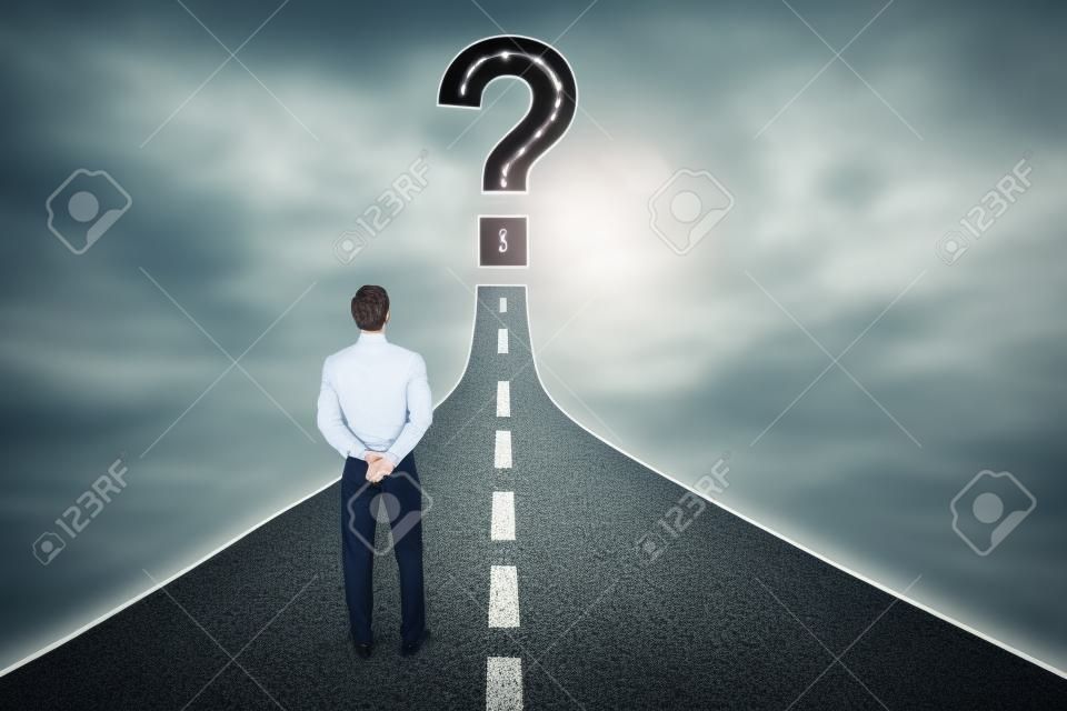 Rear view of young businessman standing on the road while looking at question sign