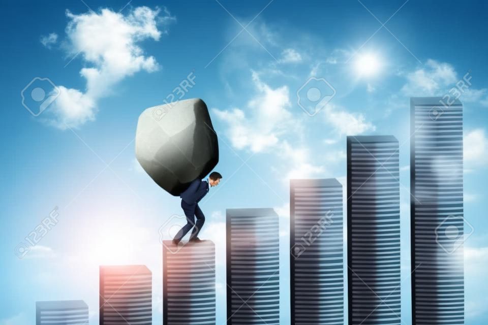 Young businessman walking on the financial chart while carrying a big stone. Concept of hard work