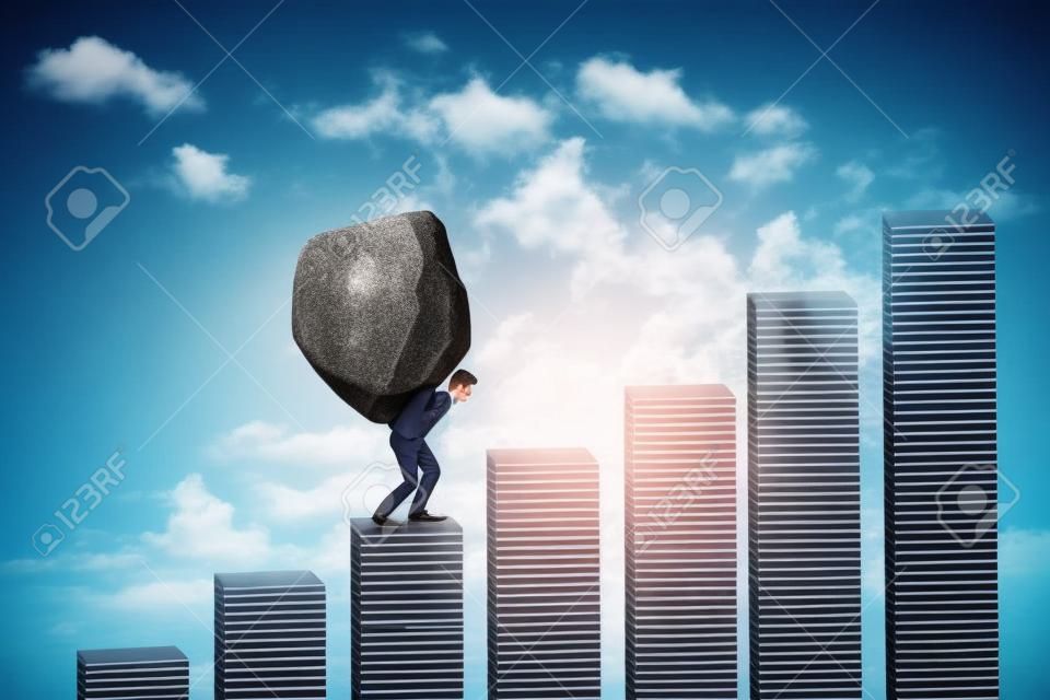 Young businessman walking on the financial chart while carrying a big stone. Concept of hard work