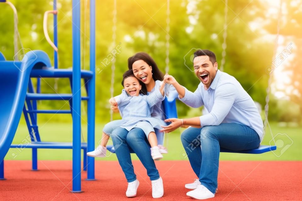 Ritratto della famiglia allegra che gioca insieme nel campo da giuoco mentre sorridendo alla macchina fotografica