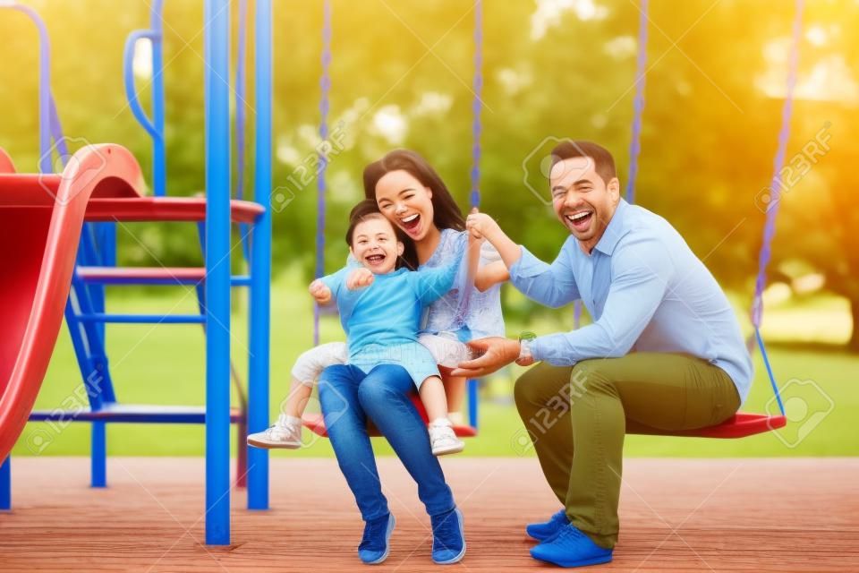 Ritratto della famiglia allegra che gioca insieme nel campo da giuoco mentre sorridendo alla macchina fotografica