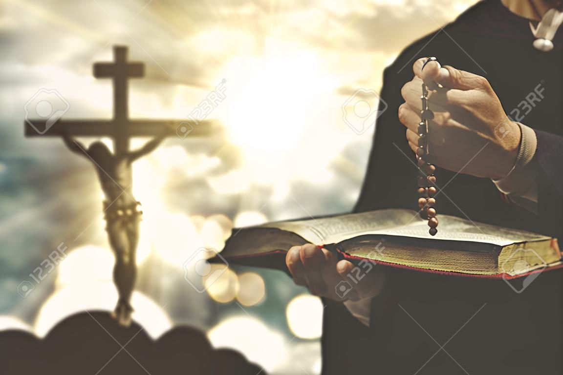 La persona cristiana che tiene una bibbia e un rosario con la crocifissione firmano sui precedenti