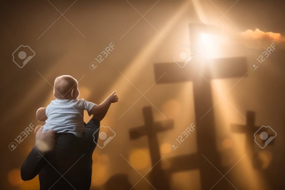 Portrait of father piggybacking his child while looking at three crucifixes under sunbeam