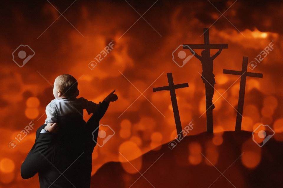 Image of father piggybacking his child while pointing at three crucifixes in the hill
