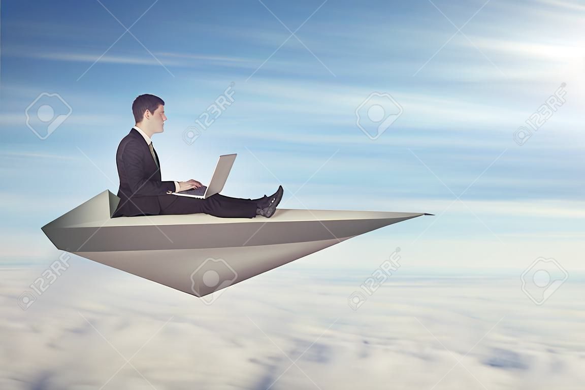 Zakenman met laptop vliegen op een papieren vliegtuig