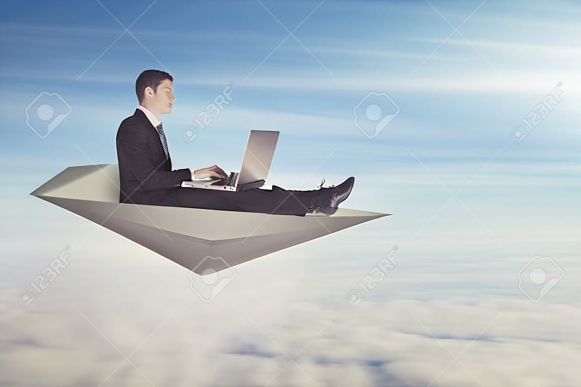 Businessman with laptop flying on a paper plane