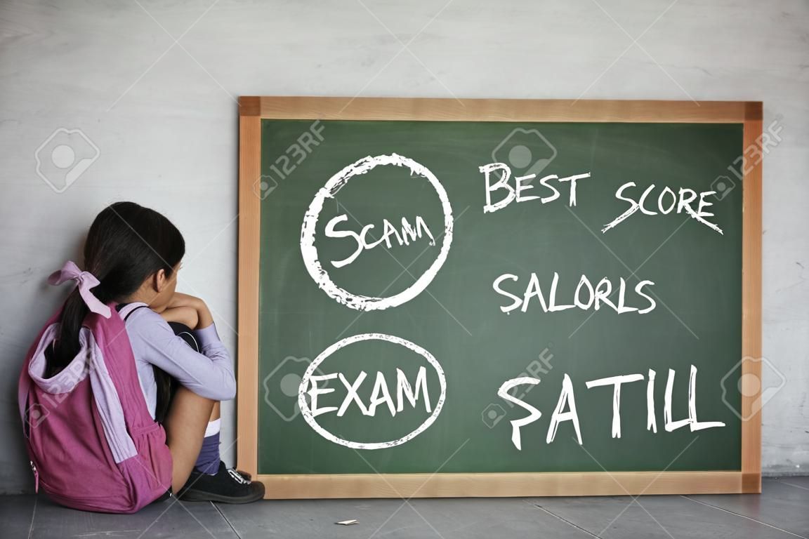 小さな女子高生のイメージは、黒板に彼女の失敗した試験のスコアと座っている間悲しそうに見えます
