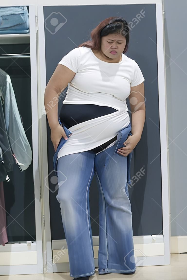 Portrait of an Asian obese woman trying to wear tight jeans and standing in the dressing room