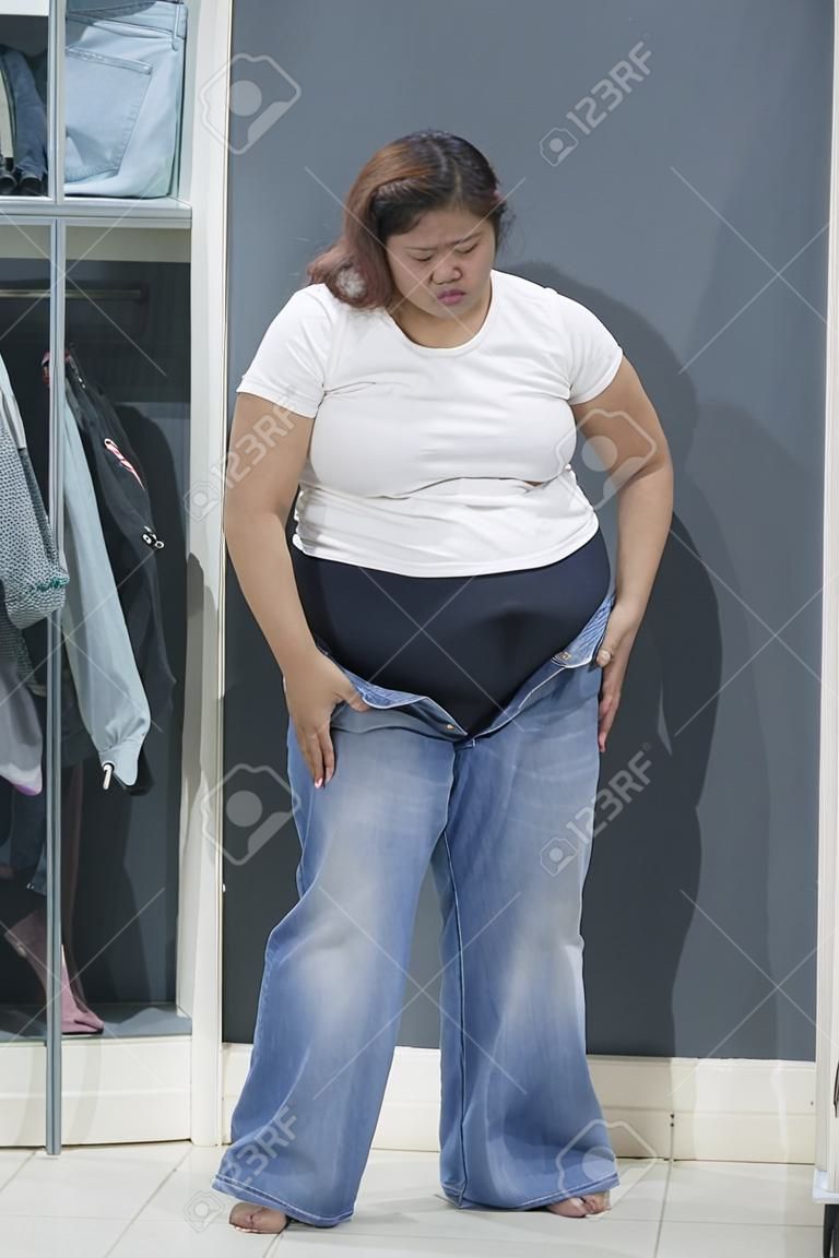 Portrait of an Asian obese woman trying to wear tight jeans and standing in the dressing room