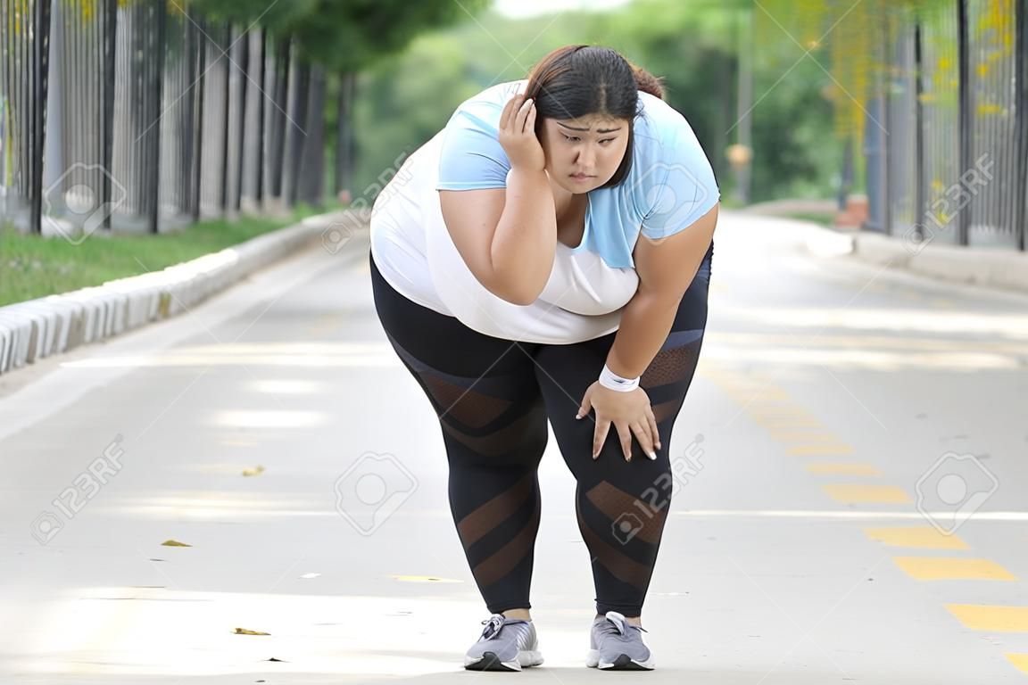 Picture of overweight woman looks tired after jogging on the road while wiping her sweat