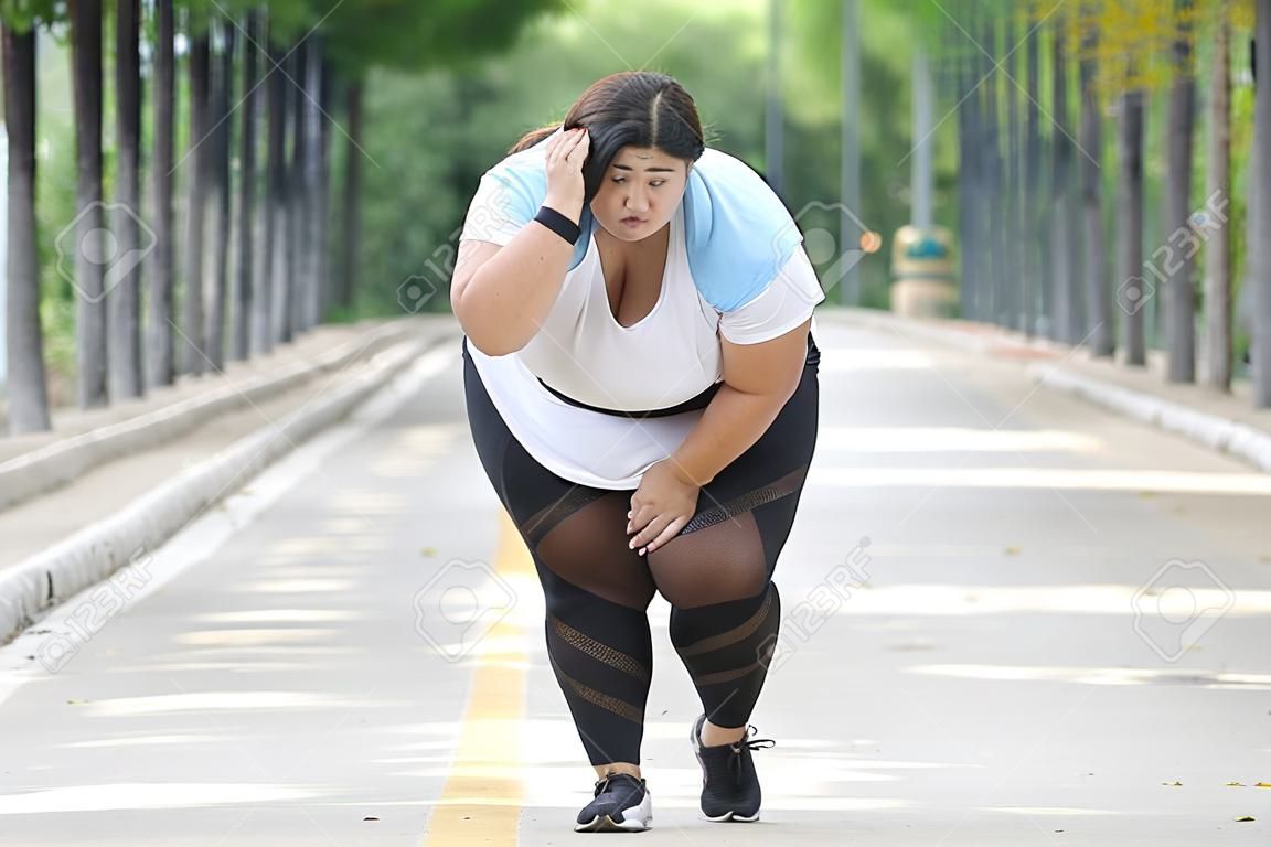 Picture of overweight woman looks tired after jogging on the road while wiping her sweat
