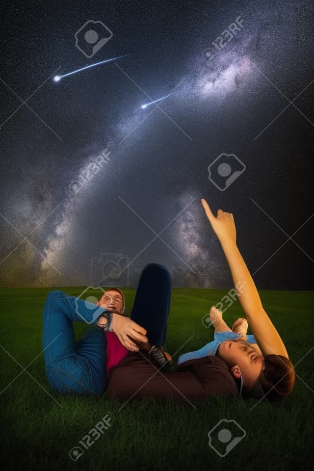 Zbliżenie na romantyczną parę leżącą razem na łące, oglądając deszcz gwiazd i Drogę Mleczną na nocnym niebie