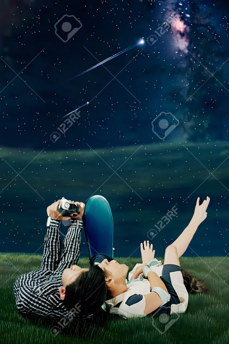 Nahaufnahme eines romantischen Paares, das zusammen auf der Wiese liegt, während es den Sternenschauer und die Milchstraße am Nachthimmel beobachtet