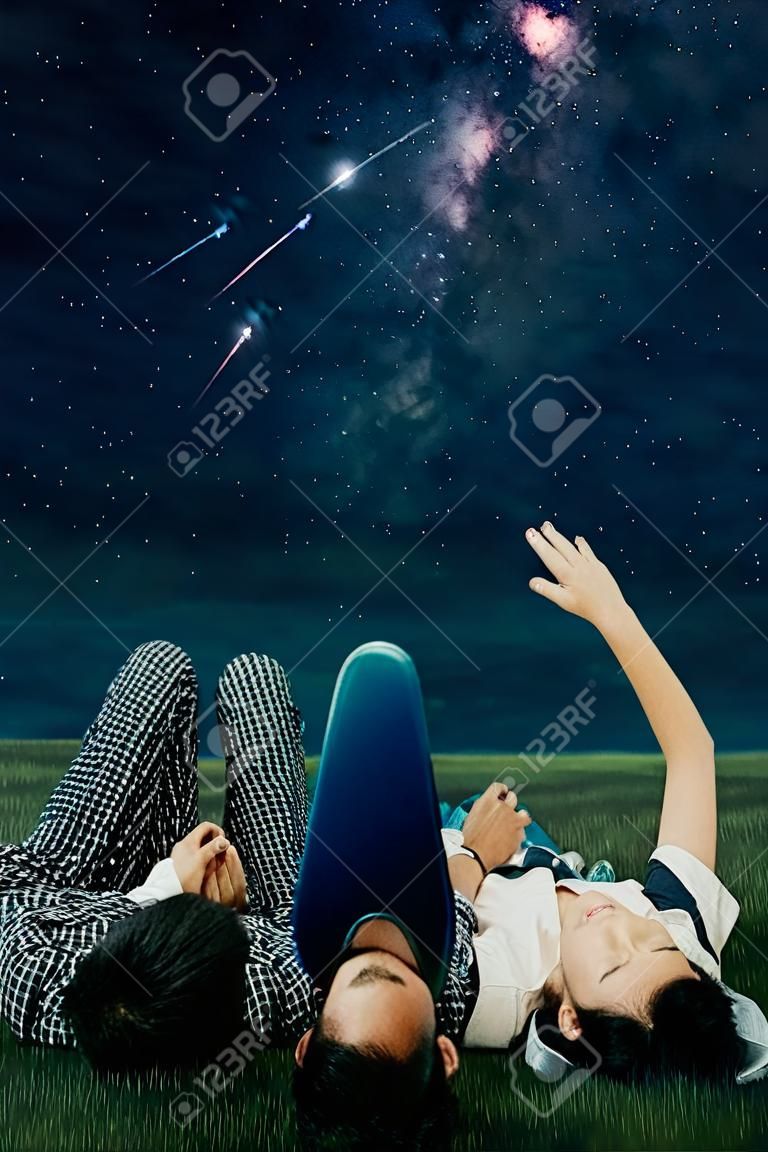 夜空に星群と天の川を見ながら、牧草地に一緒に横たわっているロマンチックなカップルのクローズアップ