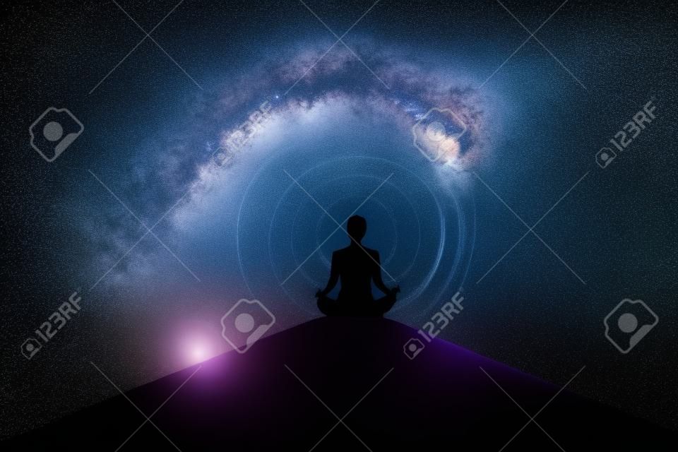 Silhouette of young woman doing yoga exercise on the mountain while meditating with milky way background. Shot in the metaverse
