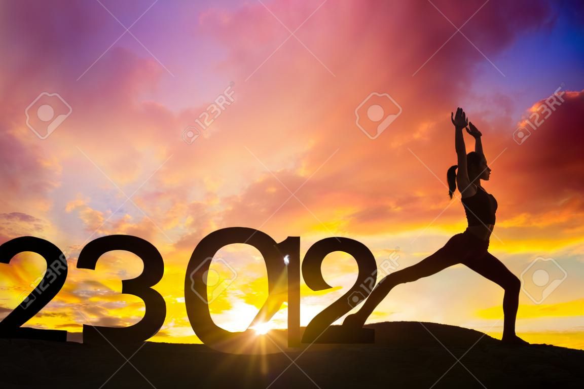일출 시간에 언덕에서 2024년 새해 숫자로 요가를 운동하는 여성의 실루엣
