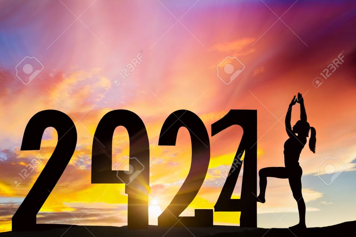 일출 시간에 언덕에서 2024년 새해 숫자로 요가를 운동하는 여성의 실루엣