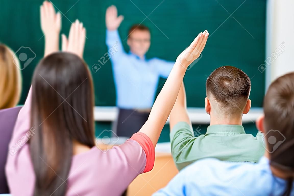 Joven estudiante femenina en un grupo levanta su brazo con el fin de responder a la pregunta.