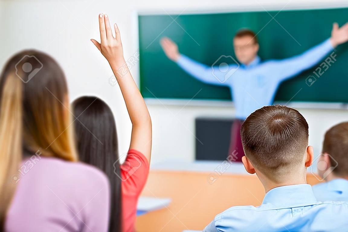 Joven estudiante femenina en un grupo levanta su brazo con el fin de responder a la pregunta.