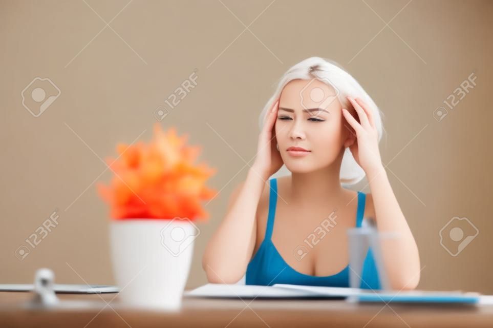 Many tasks to do. Tired pleasant attractive woman touching her head and feeling tired while sitting at  the table