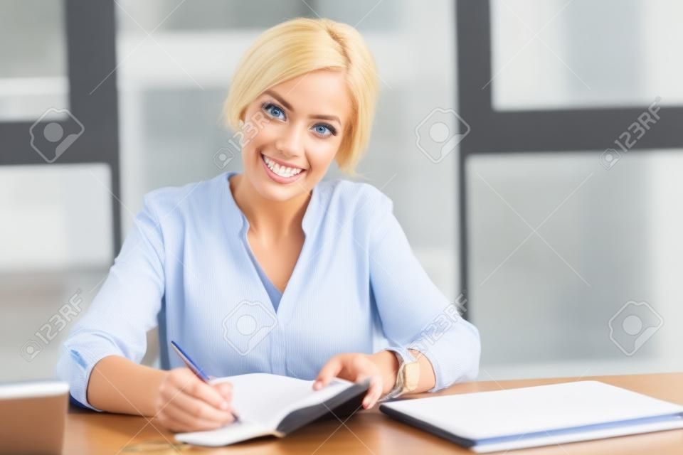 Executive worker. Confident blonde keeping smile on her face and opening her notebook while looking straight at camera
