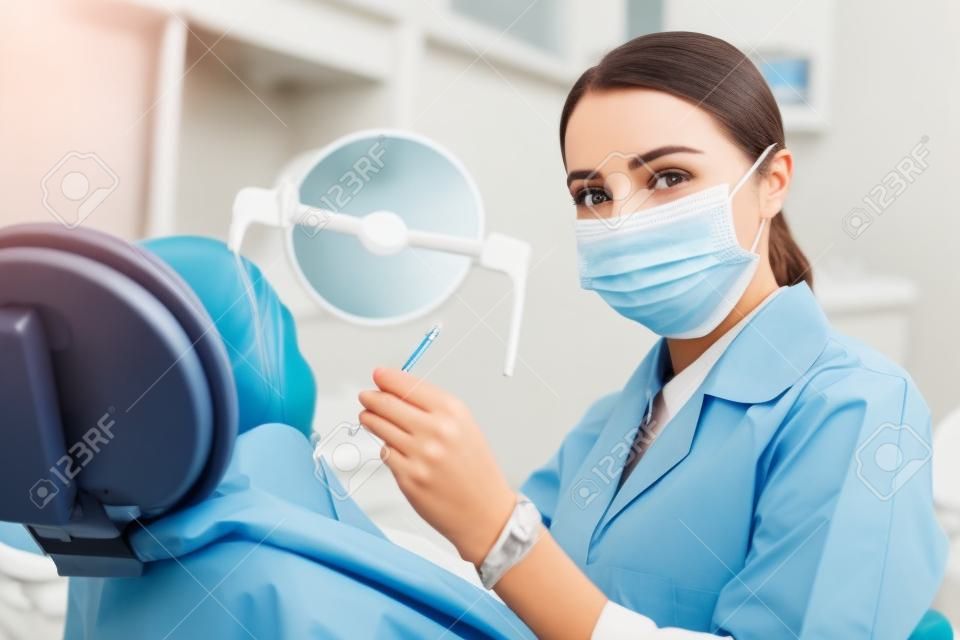 환자를 치료하는 동안 마스크를 쓰고 얼굴을 가리는 치과 치료 매력적인 여성