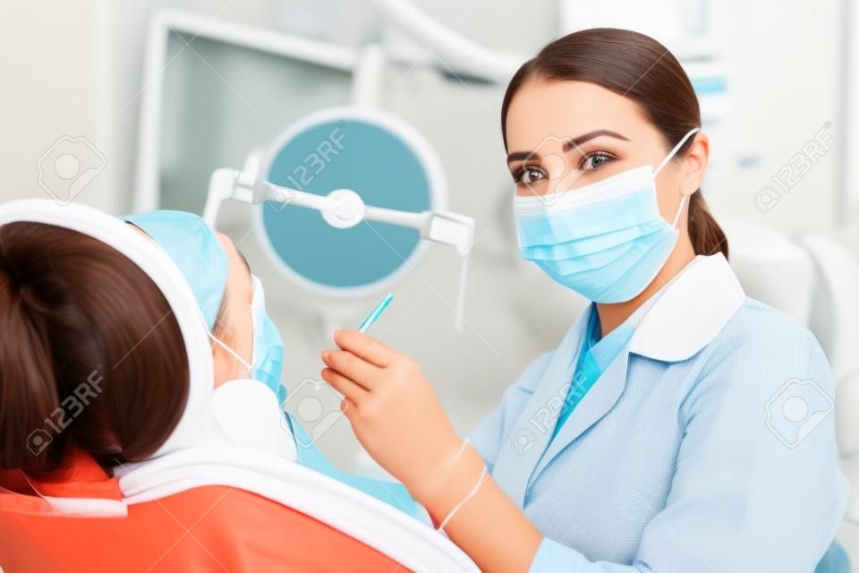 환자를 치료하는 동안 마스크를 쓰고 얼굴을 가리는 치과 치료 매력적인 여성