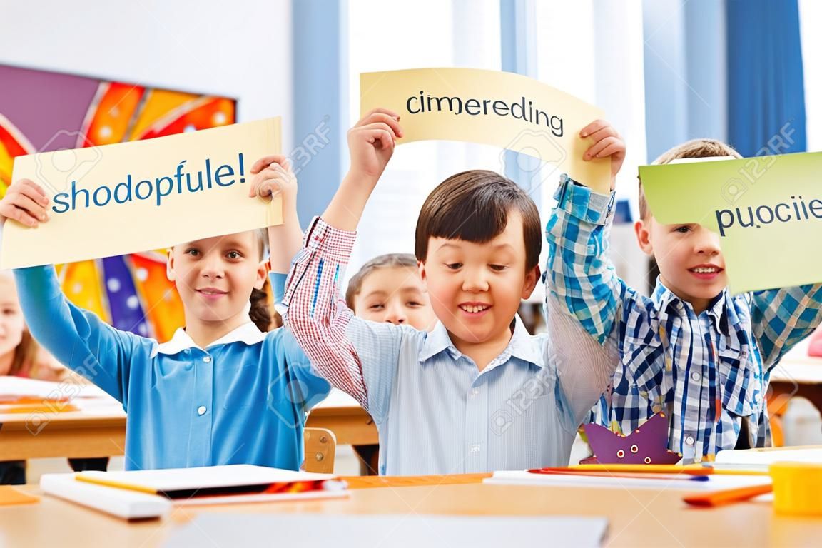 Temps d'étude. Des écoliers souriants et joyeux debout au milieu d'une salle de classe tout en tenant des tables dans leurs mains