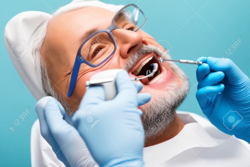 Exame dos dentes. Feche acima do paciente sênior que abre sua boca enquanto o médico qualificado segura instrumentos dentais e verifica a cavidade bucal dos pacientes