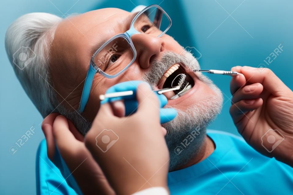 Exame dos dentes. Feche acima do paciente sênior que abre sua boca enquanto o médico qualificado segura instrumentos dentais e verifica a cavidade bucal dos pacientes