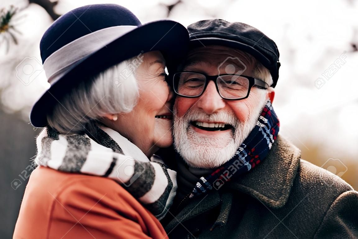 Sie ist niedlich. Glücklicher Rentner, der ein Lächeln auf seinem Gesicht behält, während er seine Frau umarmt